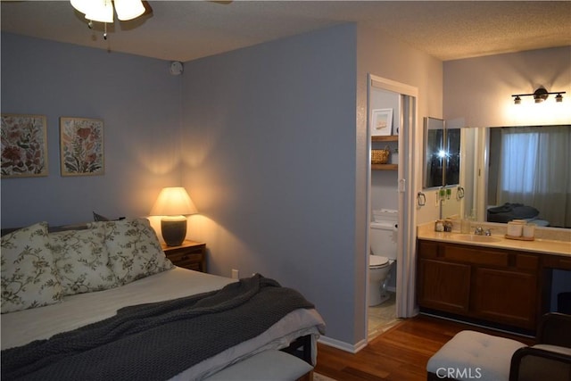 bedroom with sink, dark wood-type flooring, a textured ceiling, and connected bathroom