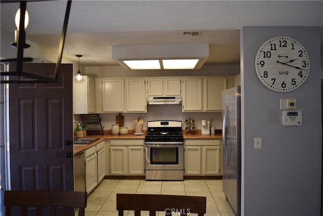 kitchen with sink, wood counters, appliances with stainless steel finishes, light tile patterned flooring, and pendant lighting