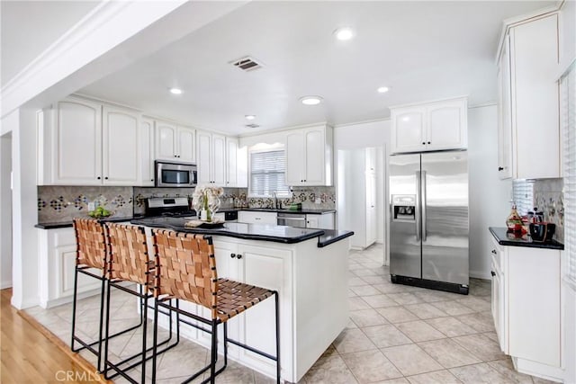 kitchen featuring stainless steel appliances, kitchen peninsula, white cabinets, and a kitchen bar