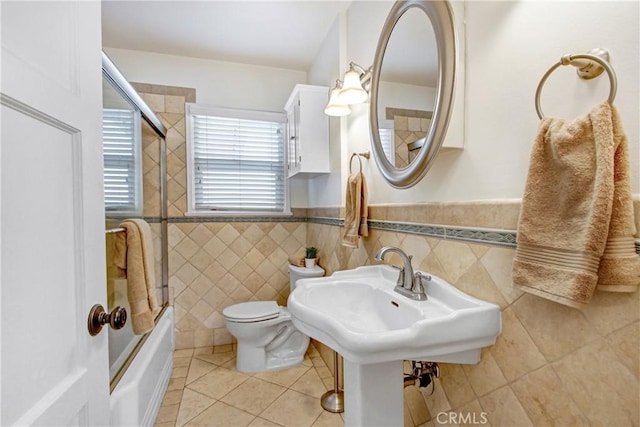 bathroom with tile patterned flooring, enclosed tub / shower combo, tile walls, and toilet