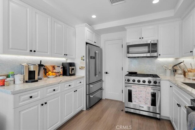 kitchen featuring tasteful backsplash, white cabinetry, high end appliances, light stone countertops, and light hardwood / wood-style flooring