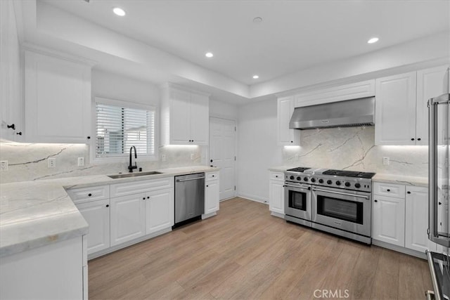 kitchen featuring sink, white cabinetry, stainless steel appliances, light hardwood / wood-style floors, and wall chimney exhaust hood