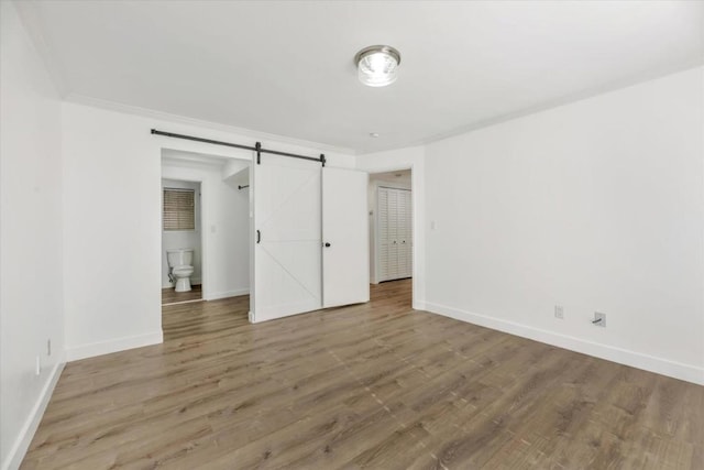 unfurnished bedroom with crown molding, wood-type flooring, and a barn door