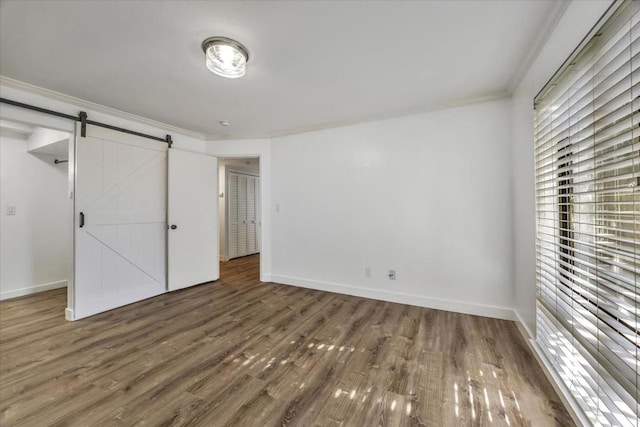 unfurnished bedroom with dark hardwood / wood-style floors, ornamental molding, and a barn door