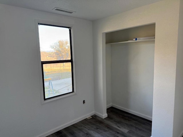 unfurnished bedroom featuring dark wood-type flooring, a textured ceiling, and a closet