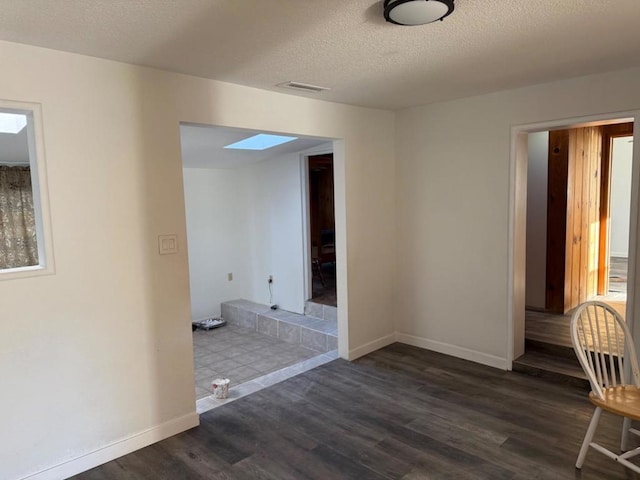 empty room featuring dark hardwood / wood-style flooring, a skylight, and a textured ceiling