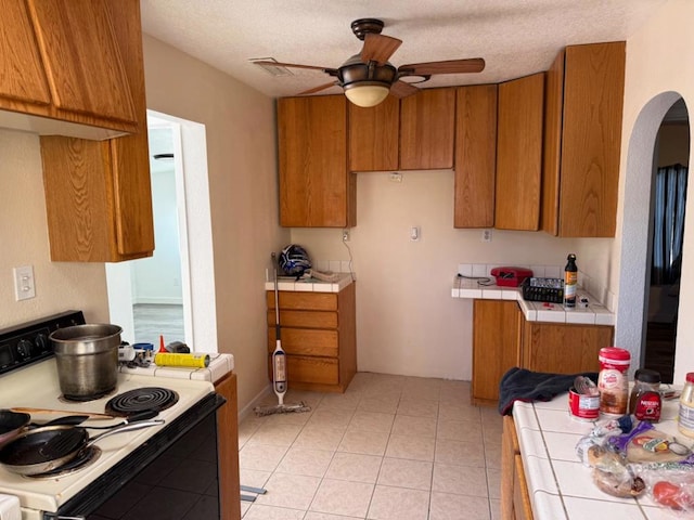 kitchen with electric stove, light tile patterned floors, tile countertops, and ceiling fan