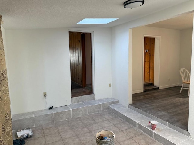 unfurnished room with a skylight, tile patterned flooring, and a textured ceiling