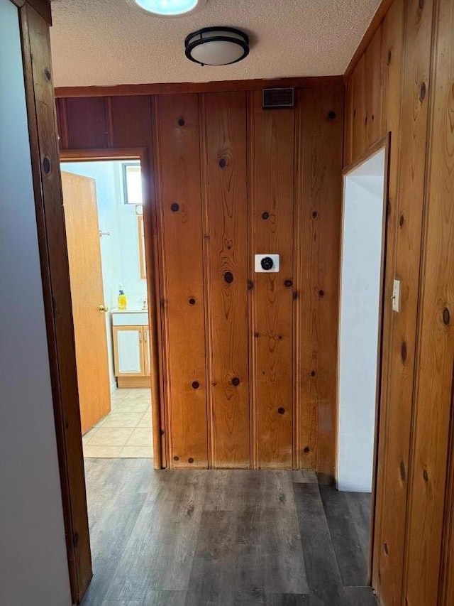 hallway featuring wood-type flooring, a textured ceiling, and wooden walls