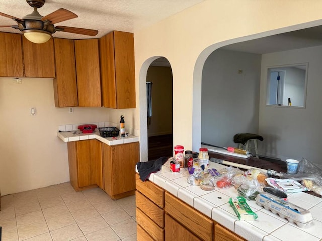 kitchen featuring a textured ceiling, tile countertops, ceiling fan, and light tile patterned flooring