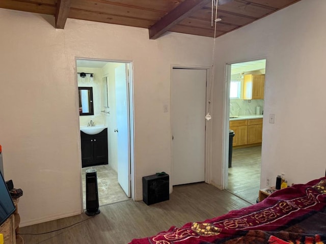 bedroom featuring beamed ceiling, ensuite bathroom, sink, and light wood-type flooring