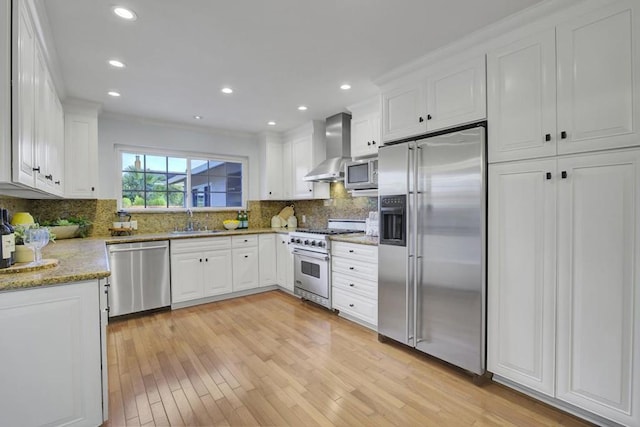 kitchen with white cabinetry, sink, backsplash, stainless steel appliances, and wall chimney range hood