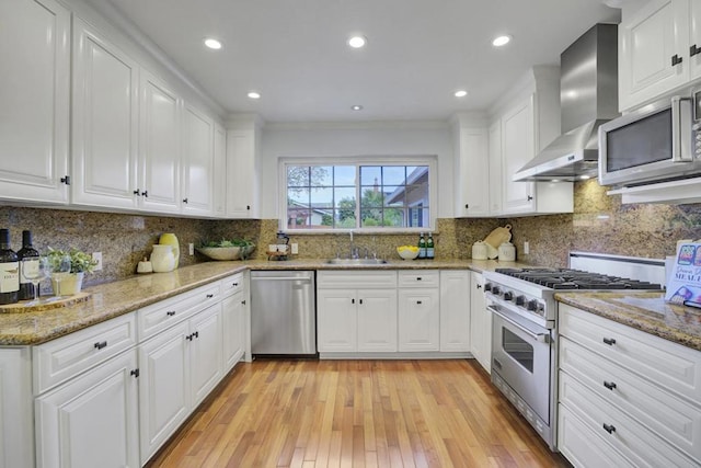 kitchen with white cabinets, appliances with stainless steel finishes, sink, and wall chimney range hood