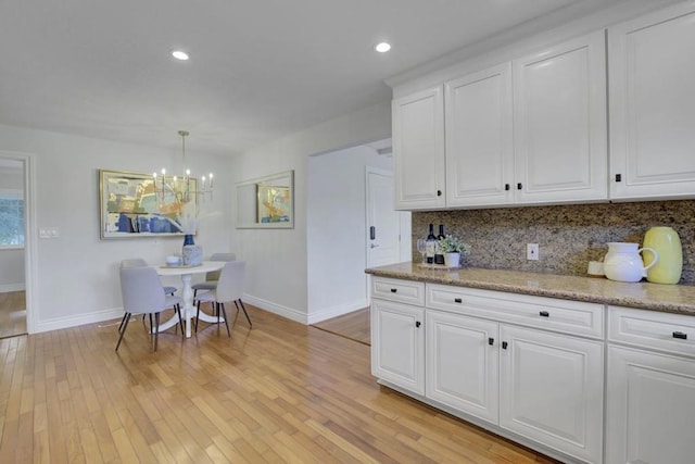 kitchen with decorative light fixtures, white cabinetry, decorative backsplash, light stone counters, and light hardwood / wood-style floors