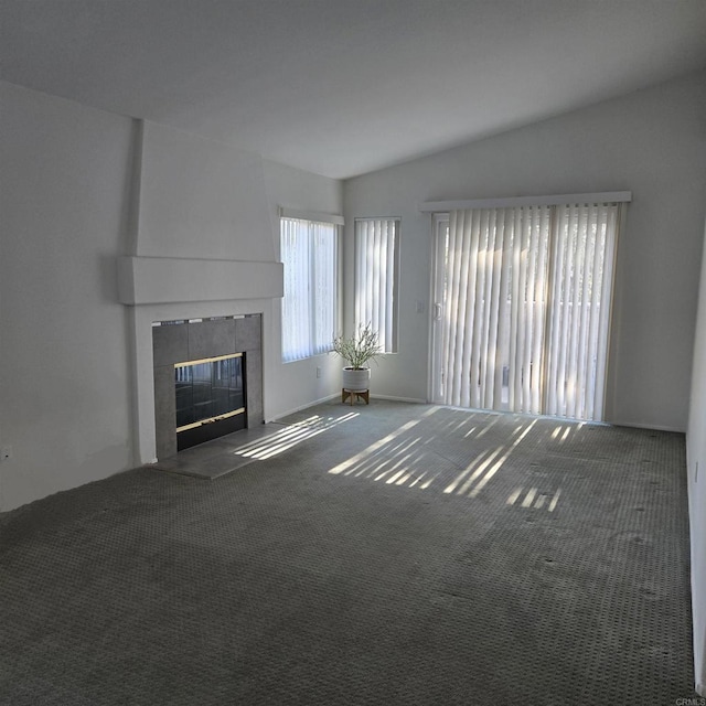 unfurnished living room featuring vaulted ceiling, a tile fireplace, and dark colored carpet