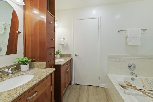 bathroom featuring hardwood / wood-style flooring, vanity, and a relaxing tiled tub