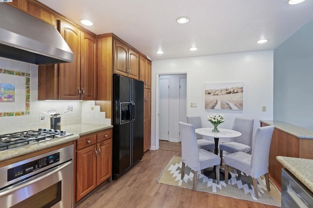 kitchen with stainless steel appliances, extractor fan, tasteful backsplash, and light hardwood / wood-style flooring