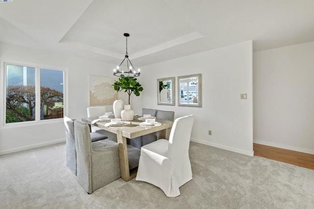 dining area with a raised ceiling, light carpet, and a notable chandelier