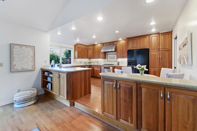 kitchen featuring sink, light hardwood / wood-style flooring, kitchen peninsula, stainless steel appliances, and wall chimney range hood