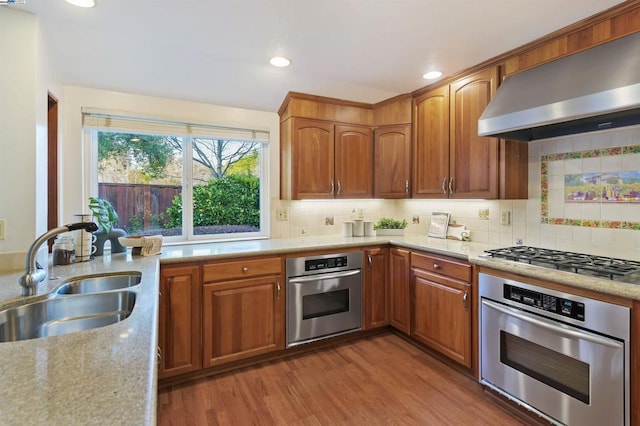 kitchen featuring sink, decorative backsplash, stainless steel appliances, light wood-type flooring, and wall chimney exhaust hood