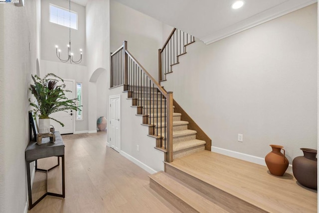 stairway featuring a towering ceiling, wood-type flooring, and a chandelier