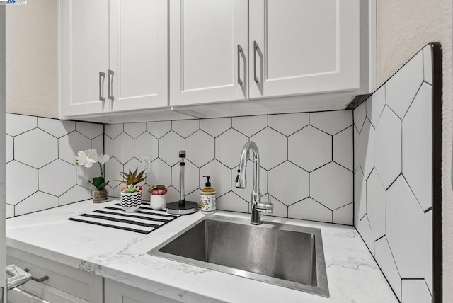 room details featuring light stone countertops, sink, white cabinets, and decorative backsplash