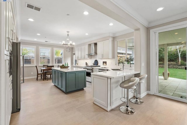 kitchen featuring high end stove, white cabinets, decorative light fixtures, kitchen peninsula, and wall chimney exhaust hood