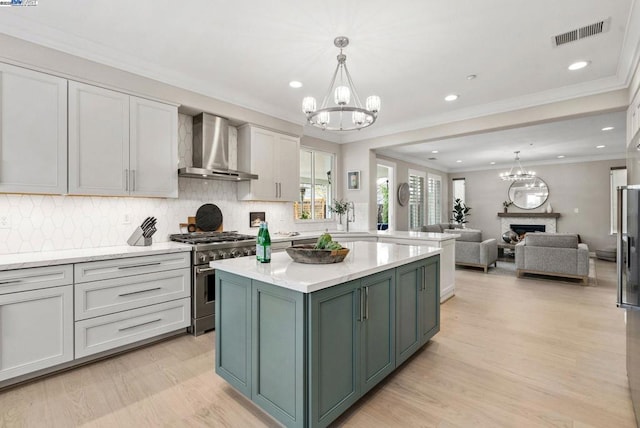 kitchen with wall chimney exhaust hood, high end stainless steel range, white cabinetry, a kitchen island, and a notable chandelier