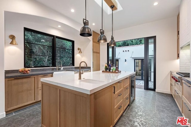 kitchen featuring pendant lighting, sink, dark stone countertops, a center island with sink, and beverage cooler