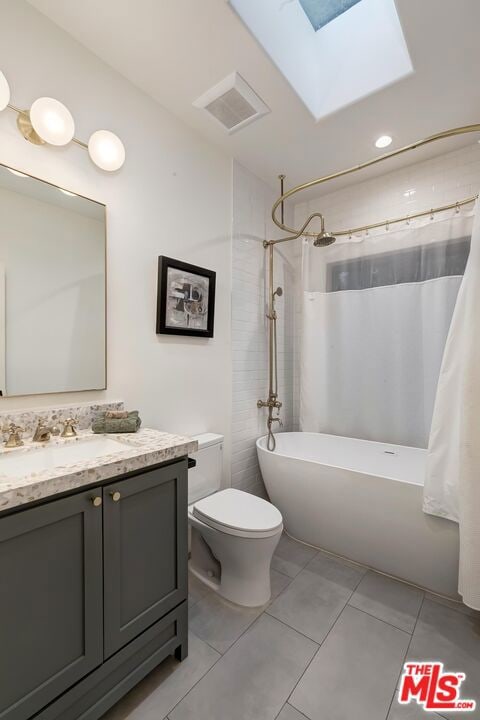 full bathroom featuring a skylight, tile patterned flooring, vanity, shower / tub combo, and toilet