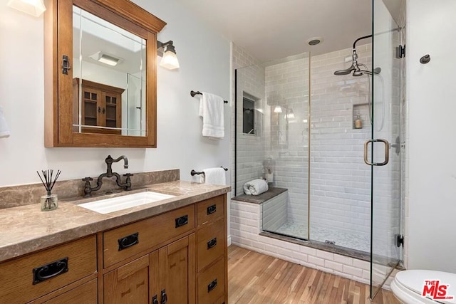 bathroom featuring wood-type flooring, walk in shower, vanity, and toilet