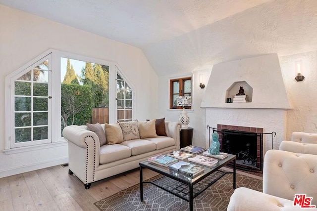 living room with lofted ceiling, hardwood / wood-style floors, a brick fireplace, and a textured ceiling