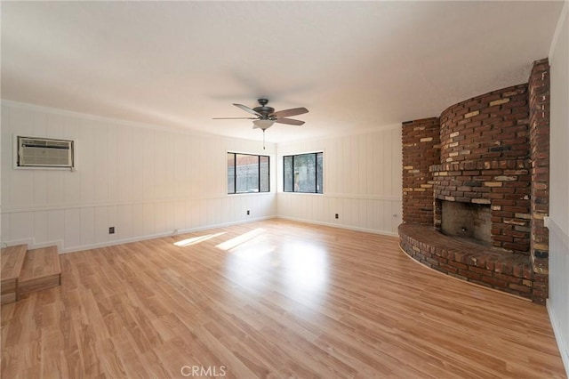 unfurnished living room featuring ceiling fan, a fireplace, a wall unit AC, and light wood-type flooring