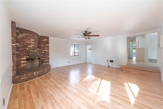 unfurnished living room with ceiling fan, ornamental molding, a fireplace, and light hardwood / wood-style flooring