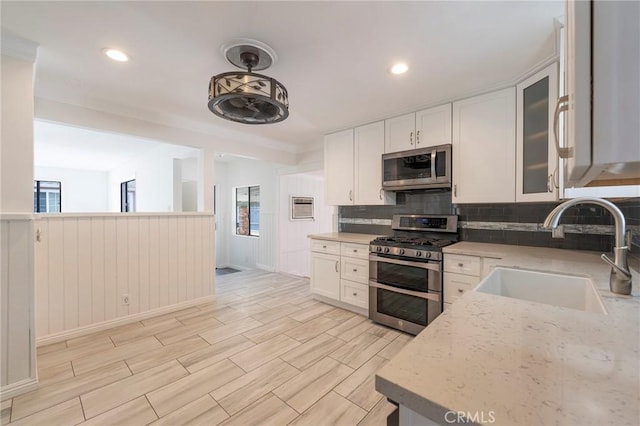 kitchen featuring sink, appliances with stainless steel finishes, light stone counters, white cabinets, and decorative light fixtures