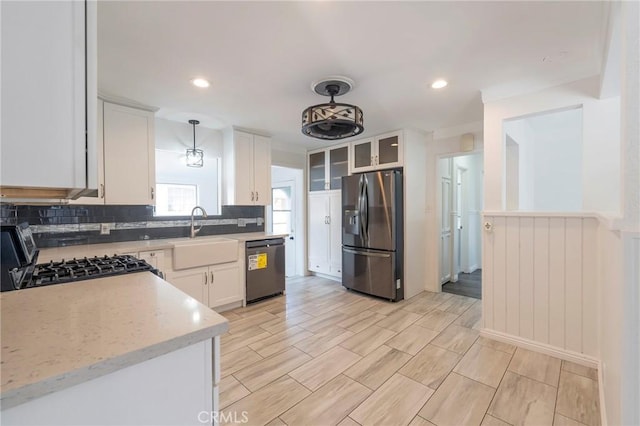 kitchen featuring sink, white cabinetry, light stone counters, pendant lighting, and stainless steel appliances