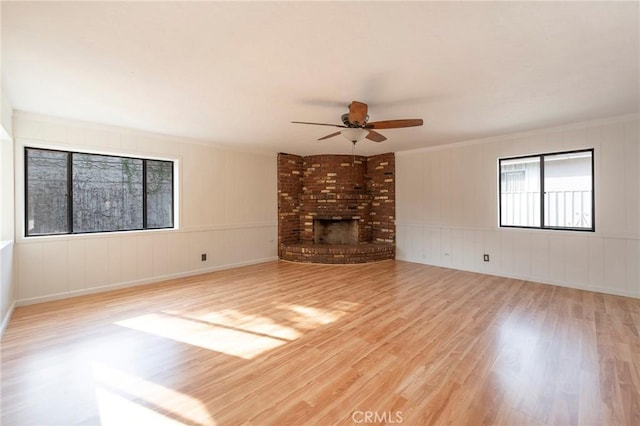 unfurnished living room with crown molding, ceiling fan, a brick fireplace, and light hardwood / wood-style flooring