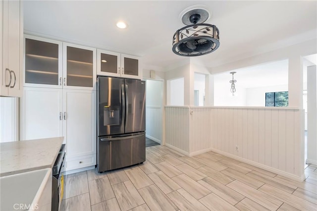 kitchen with stainless steel refrigerator with ice dispenser, sink, white cabinetry, hanging light fixtures, and light stone countertops