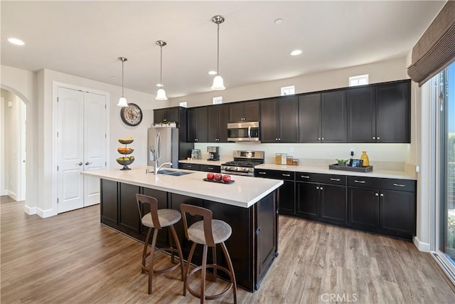 kitchen featuring a kitchen island with sink, hanging light fixtures, light hardwood / wood-style floors, and appliances with stainless steel finishes