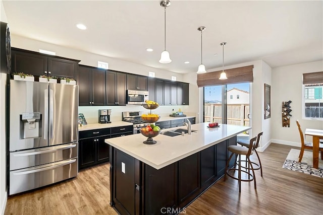 kitchen with sink, decorative light fixtures, light wood-type flooring, stainless steel appliances, and a kitchen island with sink