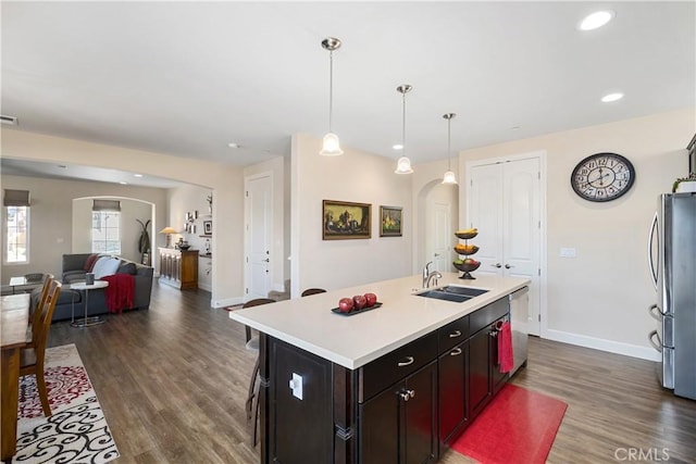 kitchen featuring sink, dark wood-type flooring, appliances with stainless steel finishes, a center island with sink, and decorative light fixtures