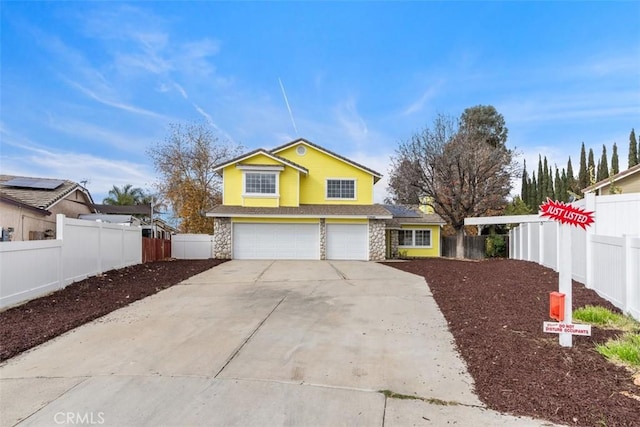 traditional home with a garage, stone siding, concrete driveway, and fence