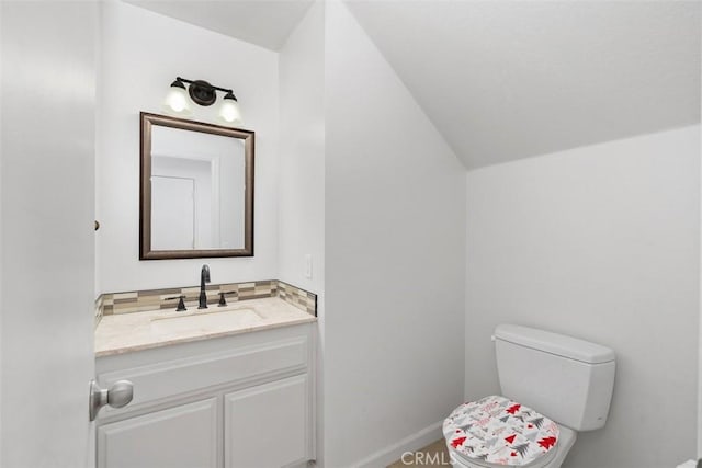 half bathroom with vaulted ceiling, toilet, vanity, and baseboards