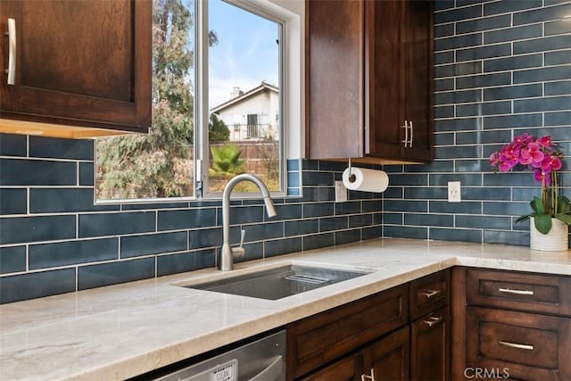 kitchen featuring tasteful backsplash, sink, light stone countertops, and dark brown cabinetry