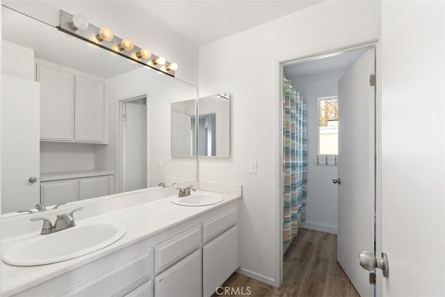 full bathroom with double vanity, a sink, baseboards, and wood finished floors