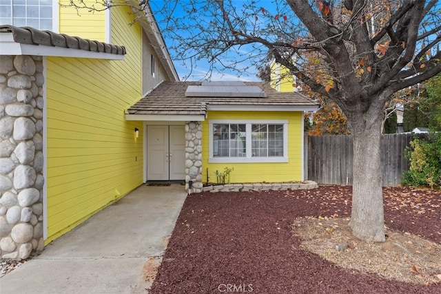 doorway to property with fence and roof mounted solar panels