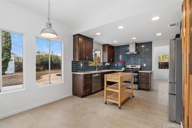 kitchen with wall chimney exhaust hood, plenty of natural light, pendant lighting, stainless steel appliances, and backsplash