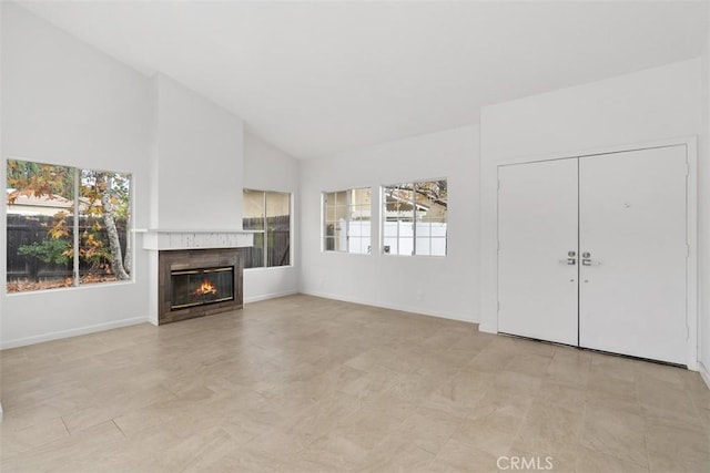 unfurnished living room featuring lofted ceiling, baseboards, and a glass covered fireplace