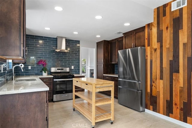 kitchen featuring sink, dark brown cabinets, appliances with stainless steel finishes, decorative backsplash, and wall chimney range hood