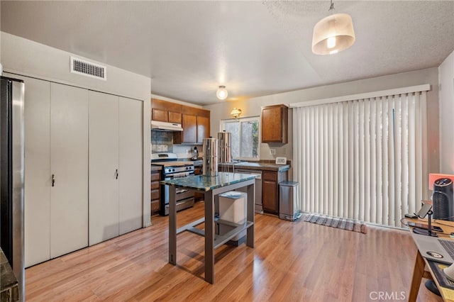 kitchen featuring stainless steel appliances, hanging light fixtures, light hardwood / wood-style flooring, a kitchen island, and a textured ceiling